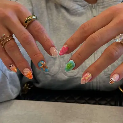 Hands displaying decorated fingernails with various artistic patterns and jewelry