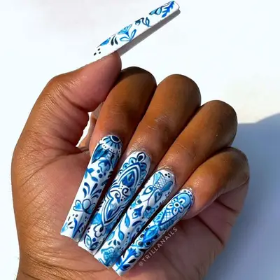A hand displaying long nails with intricate blue and white patterns