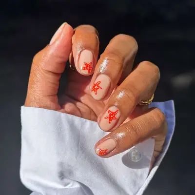 Hand with a white sleeve featuring nail art of small red designs on a beige background, rings are worn on several fingers