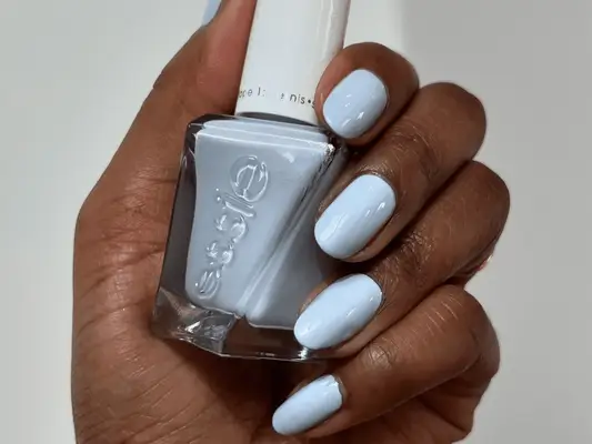 A hand holding blue nail polish with a matching blueberry milk manicure