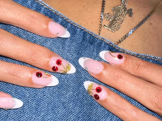 Hands with a French manicure and rhinestone cherry designs on a denim background
