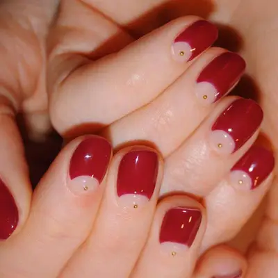 Red manicure with negative-space half moons with small gold studs