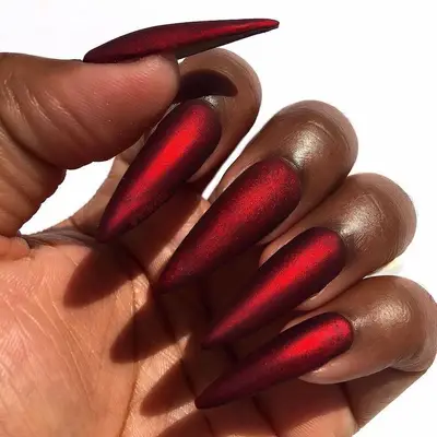 Long, pointy red acrylic nails with subtle golden shimmer