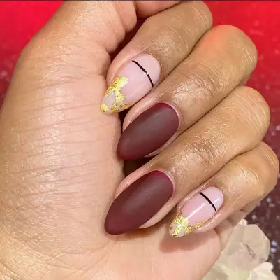 Maroon red and gold-dipped alternating nails with thin black stripe accents