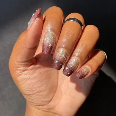 Red and gold gradient sparkle nails with moon and star charms