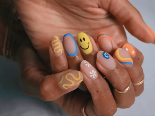 Close up of a hand with matte nails and designs like smileys and squiggles