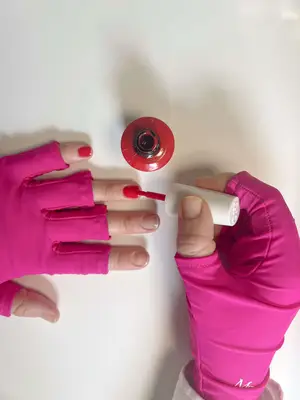 red gel polish being applied to nails with hands wearing pink UV gloves