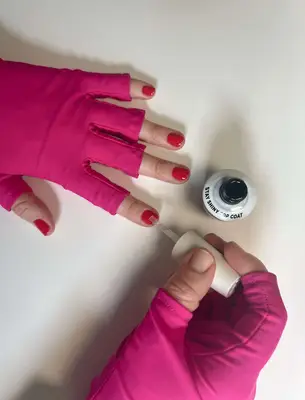 gel top coat being applied to nails wearing pink UV gloves