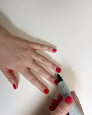 cuticle oil being applied to the cuticles of a hand wearing red nailpolish