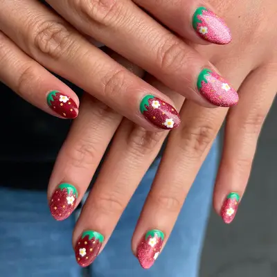 Stylish nails with strawberry-inspired designs, featuring glitter accents and floral details