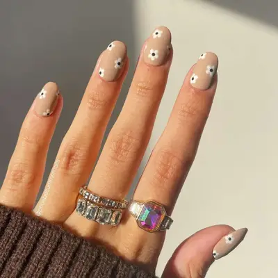Model wearing silver rings and taupe nails with white daisy design