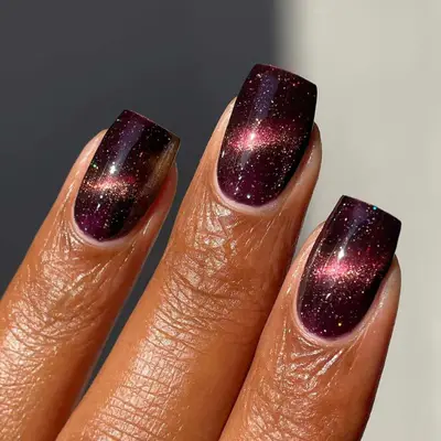 Model with maroon nails with glitter, metallic design in center