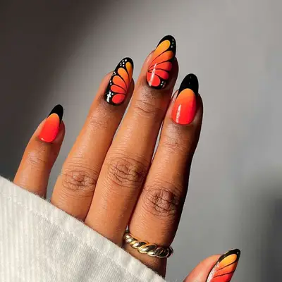 Manicure with orange ombre base, black French tips, and monarch butterfly design