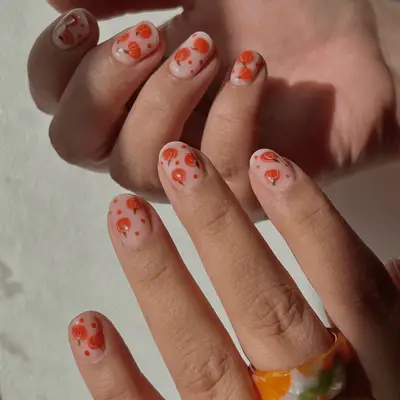 Close up of shorts nude nails with orange pumpkin nail art across each nails.