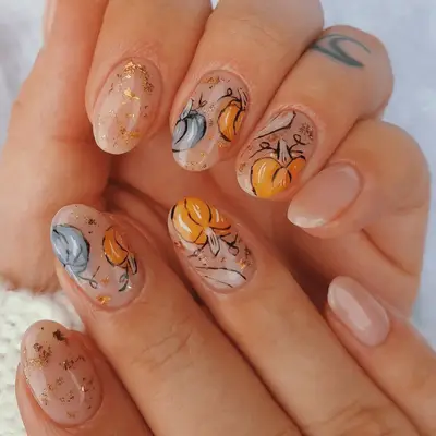 Closeup of nude nails with orange and blue watercolor pumpkin art. 
