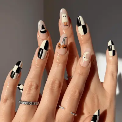 Close up of black and white checkered nails with Halloween decal accent nails, including a ghost and a cherry-stemmed Jack 