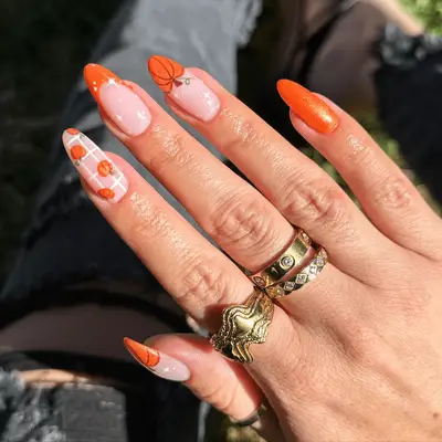 Close up of mismatched pumpkin nail art with glitter accents.