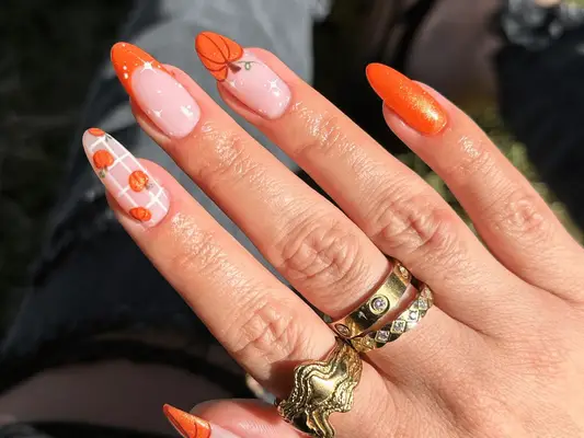 Close up of mismatched pumpkin nail art with glitter accents.