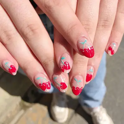 Hand with large cherries painted as the French tip of the manicure