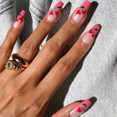 Hand with long square nails with pink French tips and a cherry design shaped like mini hearts.