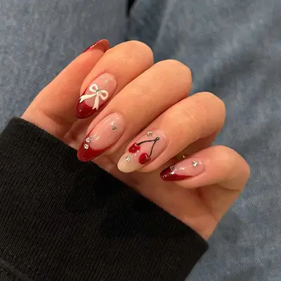 Hand with red French tips, gem stones and a cherry painted on the ring finger.