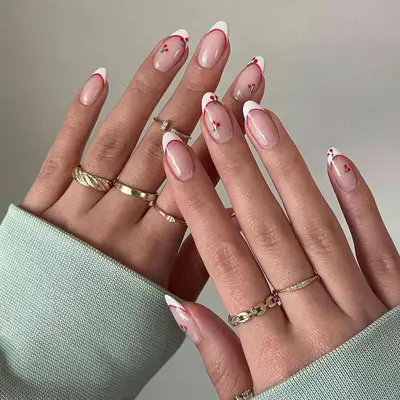 Hand with a French manicure with a red outline and mini cherry pattern.