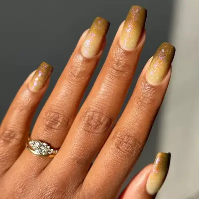 model with dark yellow nails with ombre into brown with iridescent glitter topcoat