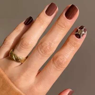 model with warm brown nails and silver sheriff charm on index finger