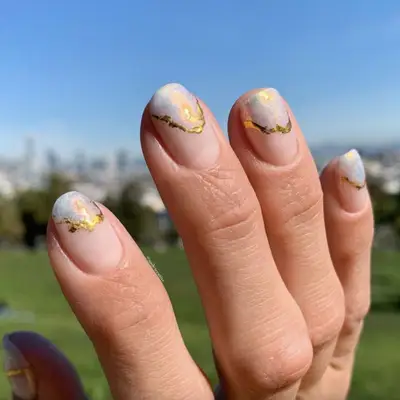 Manicure featuring iridescent stone-inspired tips with gold foil