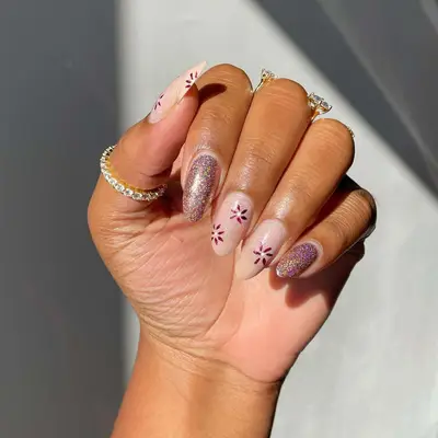close up of mails with 2 pink sparkle nails and three nails with sheer pink sparkle background and hand drawn purple flowers