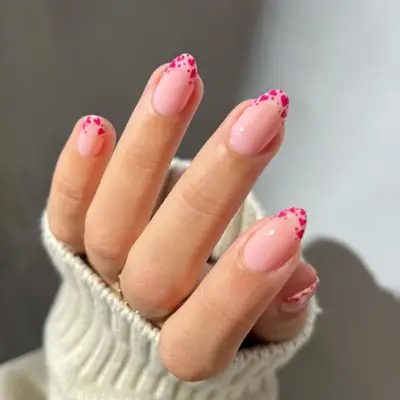 Short oval-shaped nails with a nude colored base and heart French tips in pink.