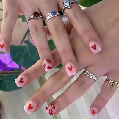 Short square nails with pink base and heart icons