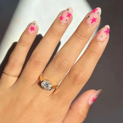 Nude short, rounded nails with a neutral base, pink stars and sparkles.