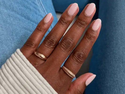 A hand with gold rings and pale pink nails and denim in the background