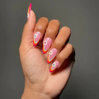 Hand with pink manicure with rainbow arched French tip and daisy nail stickers with colorful centers
