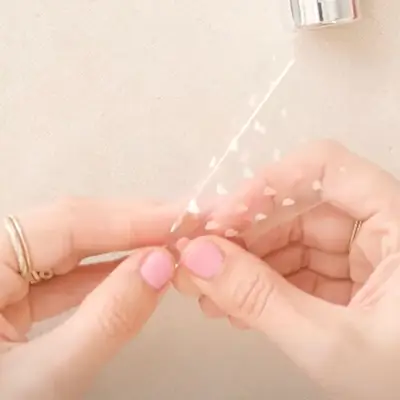 Person with pink manicure peeling heart nail stickers off a clear sheet