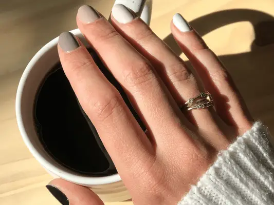 Close up of a hand with a nude ombré manicure over a cup of coffee