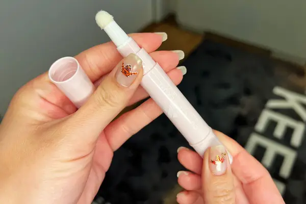 Hands holding an uncapped bottle of Olive & June Cuticle Serum Duo and its lid 