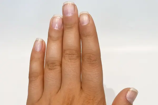 Close-up of a hand with nails treated with cuticle oil against a grey background 