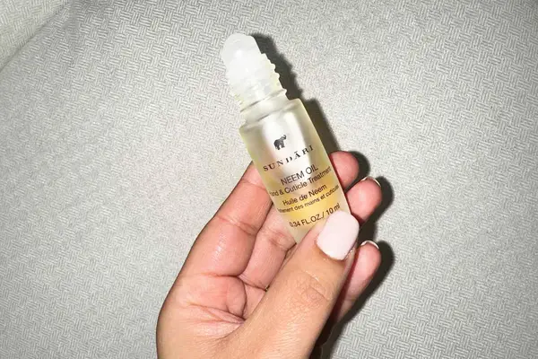 Hand holding an uncapped bottle of Sundari Neem Hand and Cuticle Hand Treatment Oil