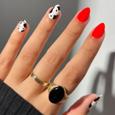Cow print nails with two neon red nails.