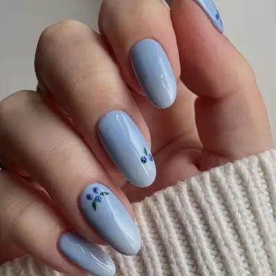 Close-up of manicure with solid pastel blue base and blueberry designs