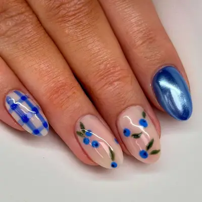 Manicure with one blue chrome nail, one blue plaid nail, and neutral nails with blueberry pattern