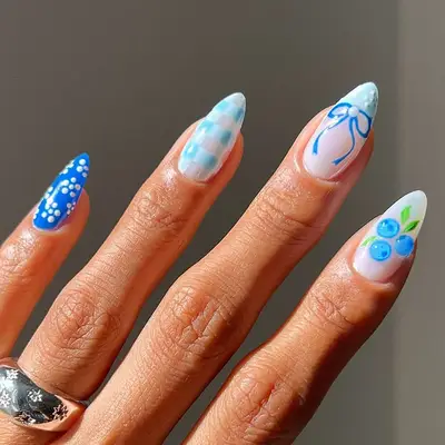 Hand with nails adorned in various blue-themed artistic designs, including patterns and small painted figures