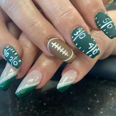 close up of nails, one painted brown with white that looks like football, other nails green with white tick marks and yardage numbers like a football field