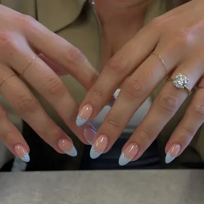 Hands with baby blue manicured nails and gold rings adorned with a diamond