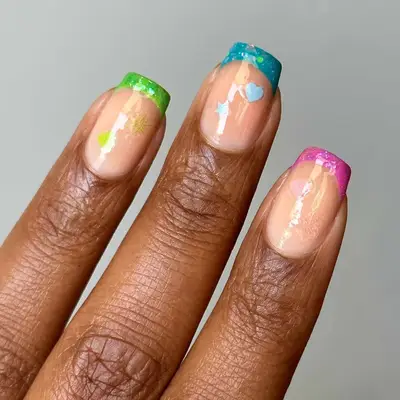A hand with nails painted in colorful tips featuring small decorative elements