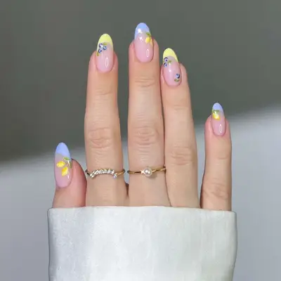 Close-up of hand with pastel-colored manicure featuring floral nail art and rings on fingers