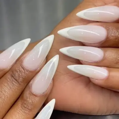 Close-up of a hand with long almond-shaped nails featuring a glossy white finish and intricate design tips