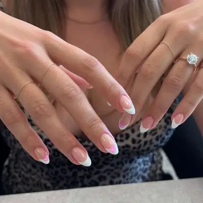 Hands displaying long manicured nails with intricate designs, wearing delicate rings and a prominent diamond ring on one finger